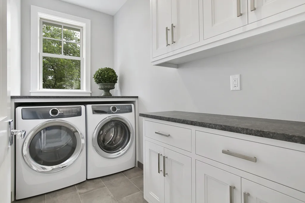 Laundry room with large rectangular tiles, white cabinets and dark countertops