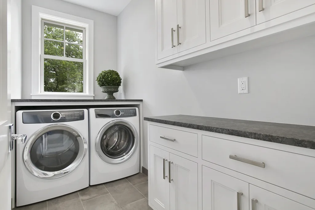 Laundry Room With Large Rectangular Tiles, White Cabinets And Dark Countertops