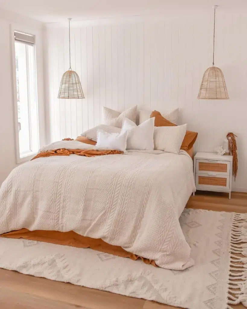 A White Bed With Orange Accents And A White Rug Underneath The Bed