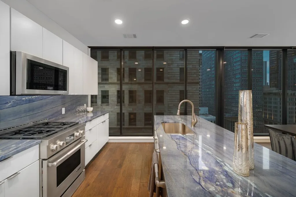 A Modern Apartment Kitchen With Grey Granite Countertops And Backsplash Including A Waterfall Island