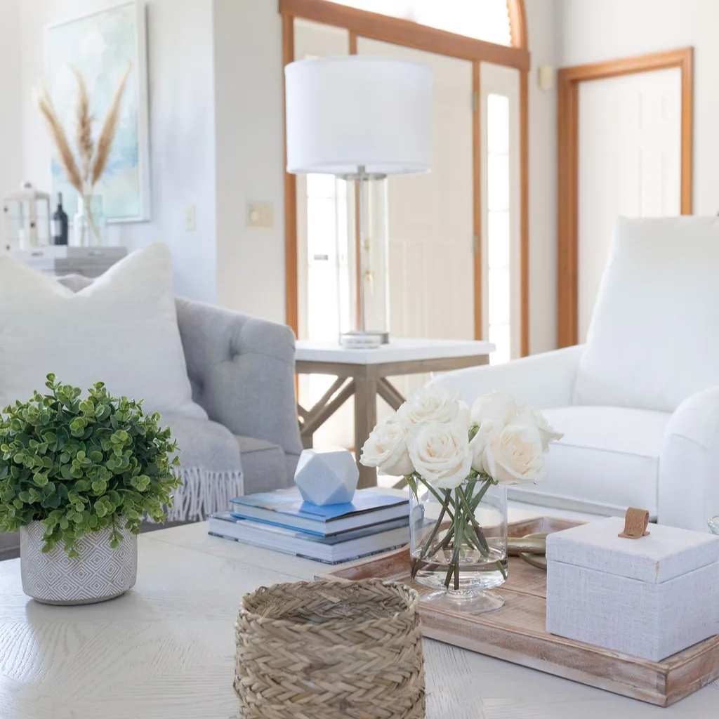A White Accent Chair Next To A Grey Sofa With White Pillows In A Beach House