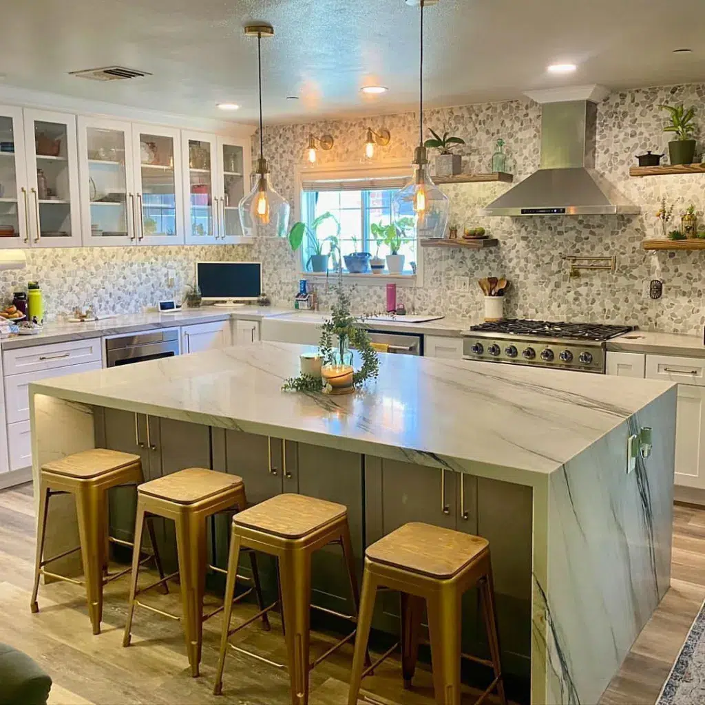 A Wide Waterfall Kitchen Island With Metal Bar Stools And Grey Cabinets Undernath