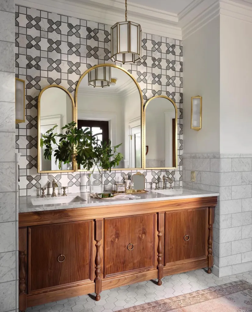 A Brown Antique Style Vanity With Mosaic Backsplash And Gold Decor Ont He Countertop That Matches The Mirrors