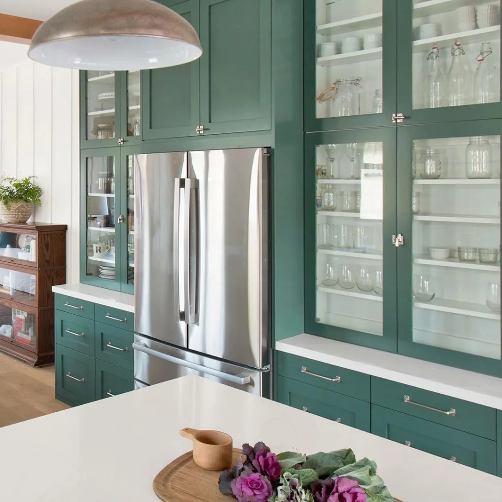Floor-To-Ceiling Green Cabinets With Glass Upper Cabinets And A Stainless Steel Fridge
