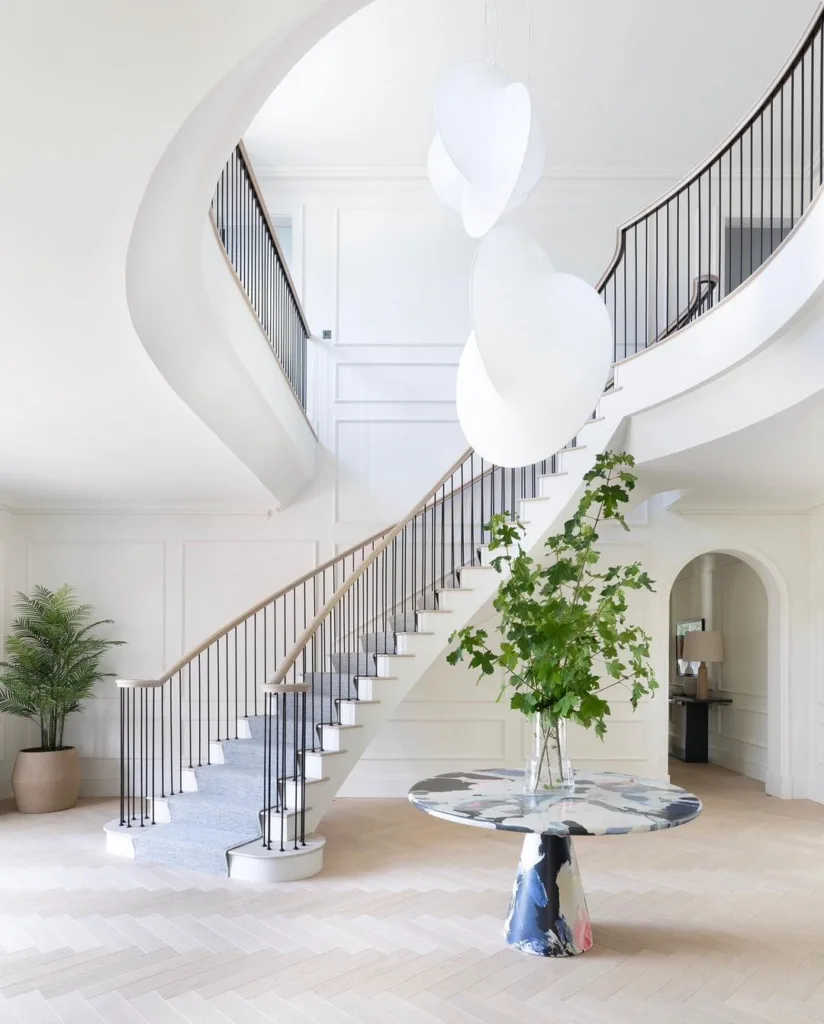 A White Entryway With Chevron Floors And A Large Curved Staircase With Metal Spindles And Wood Railings