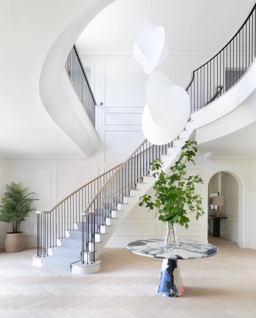 24 Curved Staircases For Design And Decor Inspiration 7 A White Entryway With Chevron Floors And A Large Curved Staircase With Metal Spindles And Wood Railings