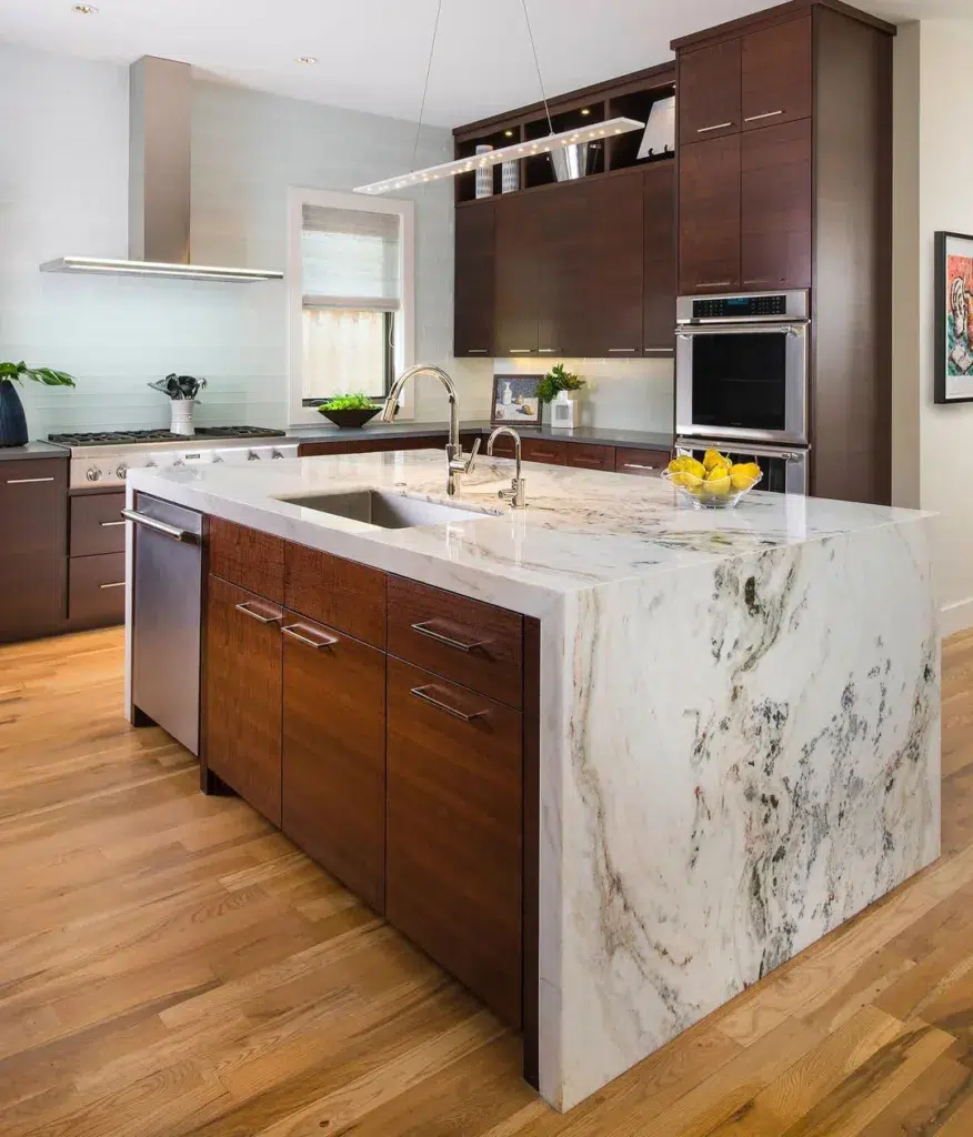 The Marble Waterfall Island Accentuated By Dark Wood Cabinets And Stainless Steel Applainces