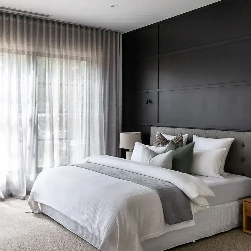 A Black Accent Wall Behind A Grey Bed With White Bedding And Light Colored Carpet