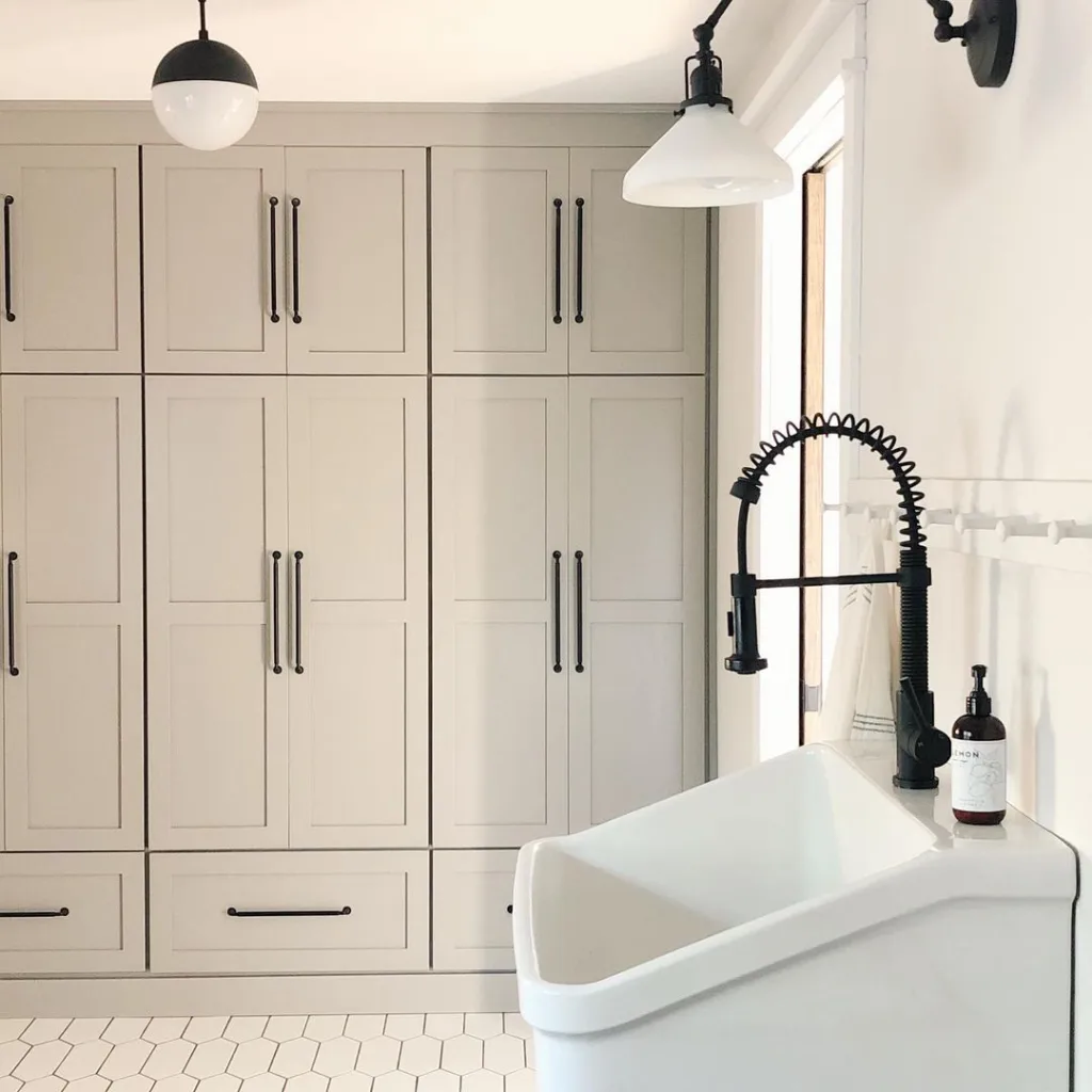 White Floor To Ceiling Cabinet Used In A Washroom With A White Sink And Black Tap. 