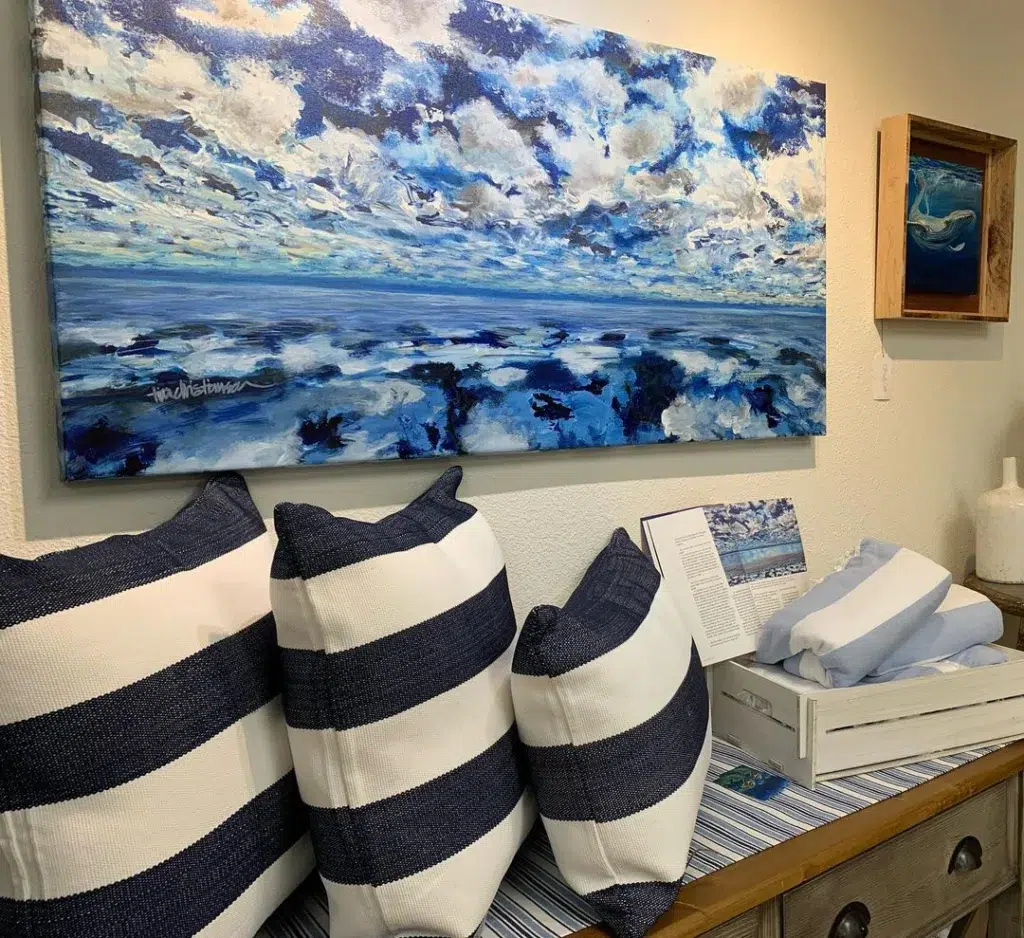 A Beach Themed Living Room Nook With Blue And White Striped Pillows And Artwork Showing The Ocean