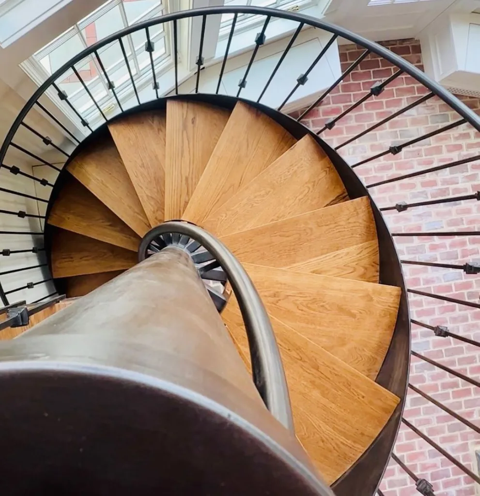 A Circular Wood Staircase With Metal Railings Leading To A Room With Brick Floors
