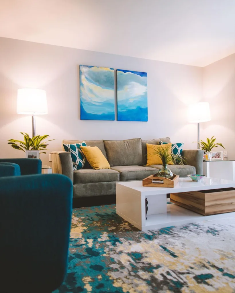 Pops Of Blue And Green With Throw Pillows, Curtains, And A Beach-Inspired Painting In This Living Room
