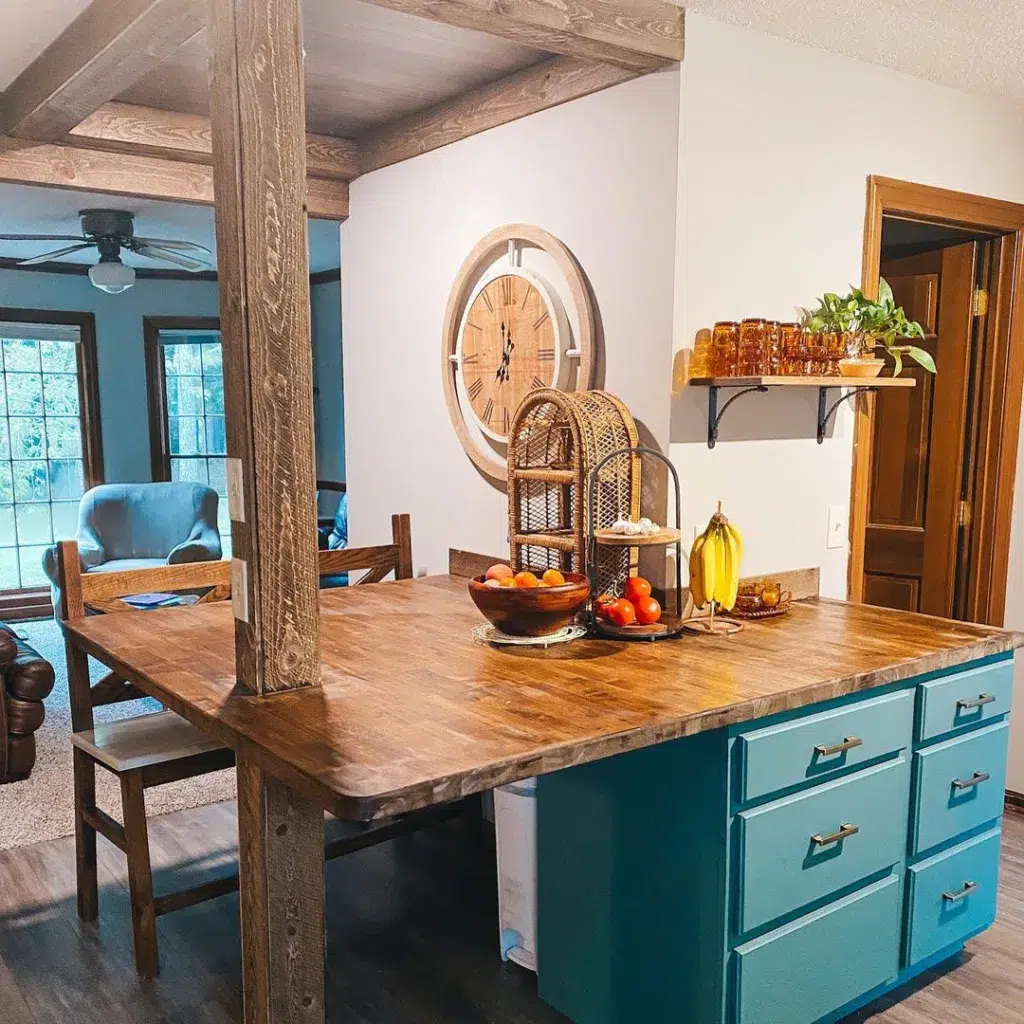A Teal Island With A Wood Countertop And Rustic Wood Beams