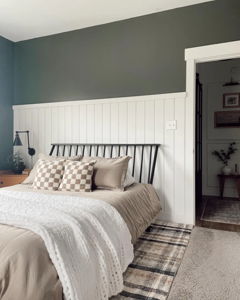 White Partial Wall Shiplap Behind A Black Metal Bed With Beige Bedding And A Plaid Rug Underneath