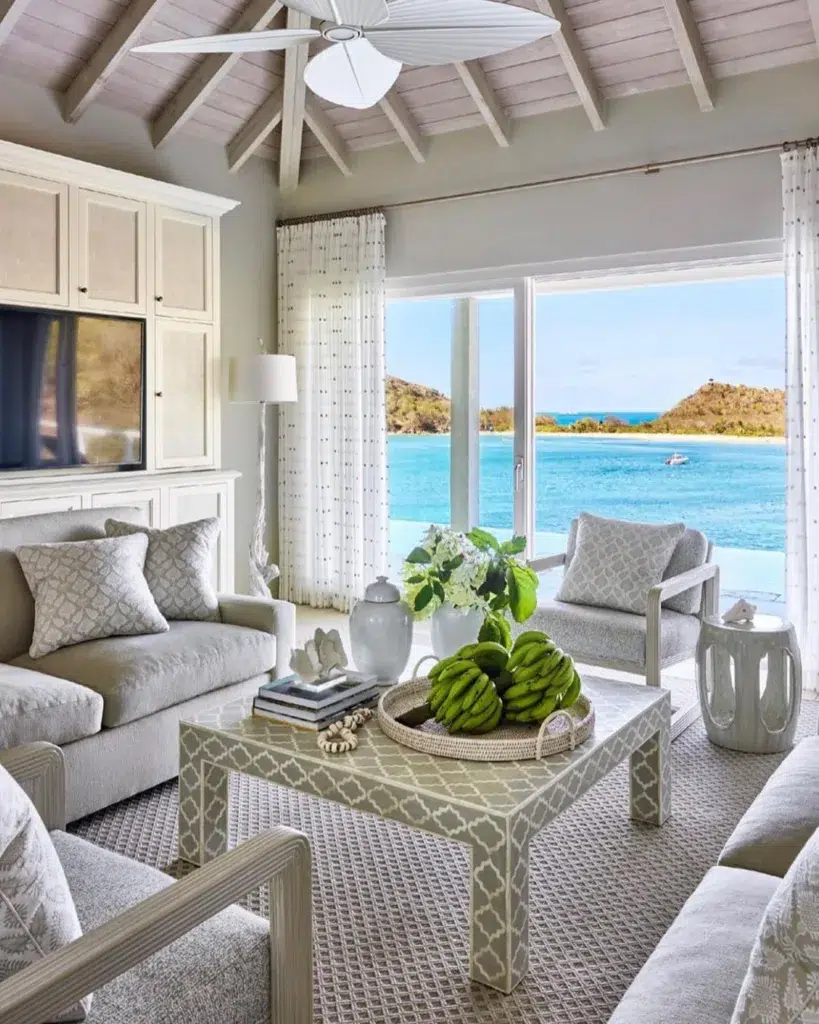 White And Grey Furniture In A Sitting Area With Large Sliding Windows Overlooking Blue Ocean Water