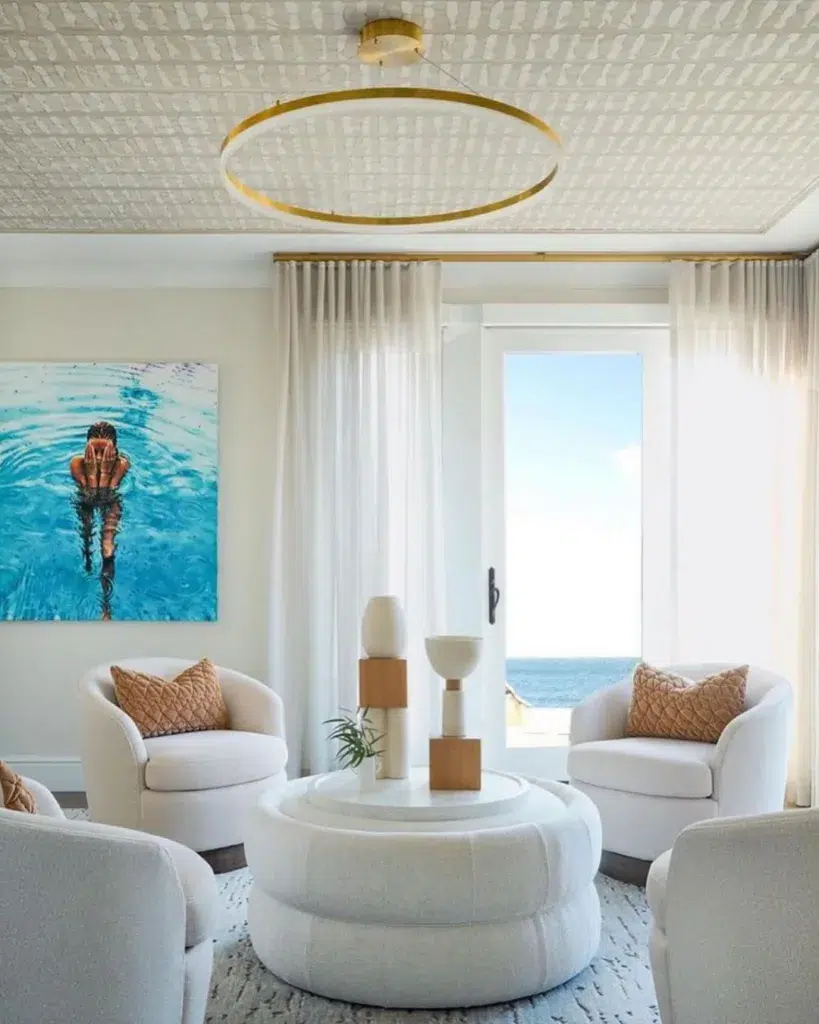 A Sitting Room With A View Of The Ocean And Four Beige Accent Chairs Arranged Around A Coffee Table