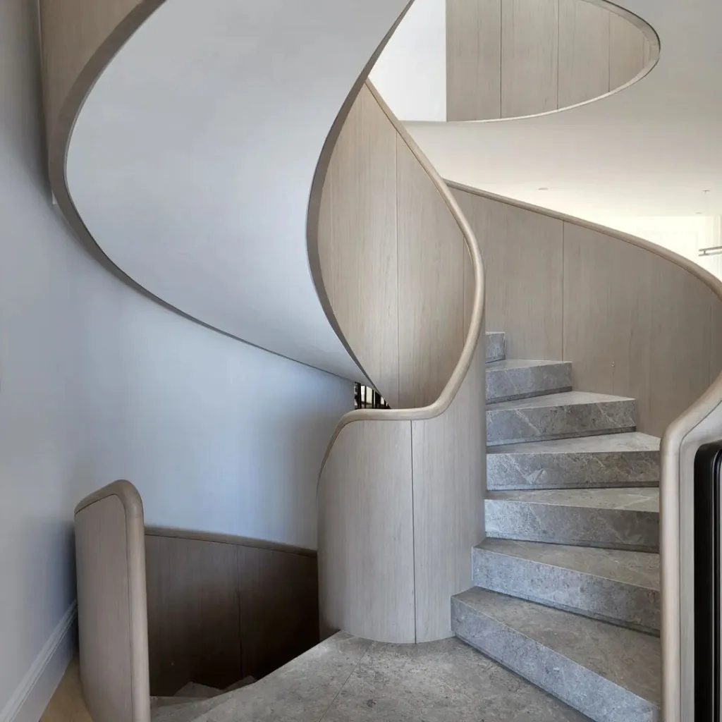 A Modern Curved Staircase With Grey Marble Steps And Wood Sides