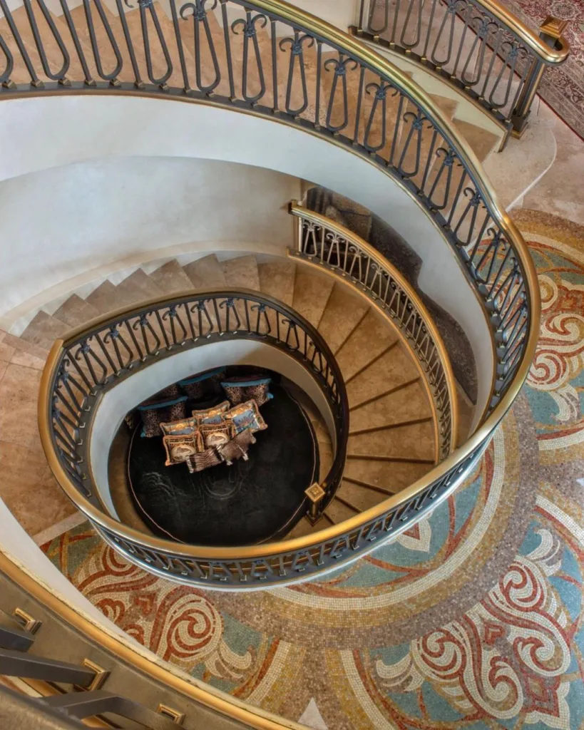 A Grand Curved Staircase With A Polished Wooden Handrail And Ornate Wrought Iron Spindles