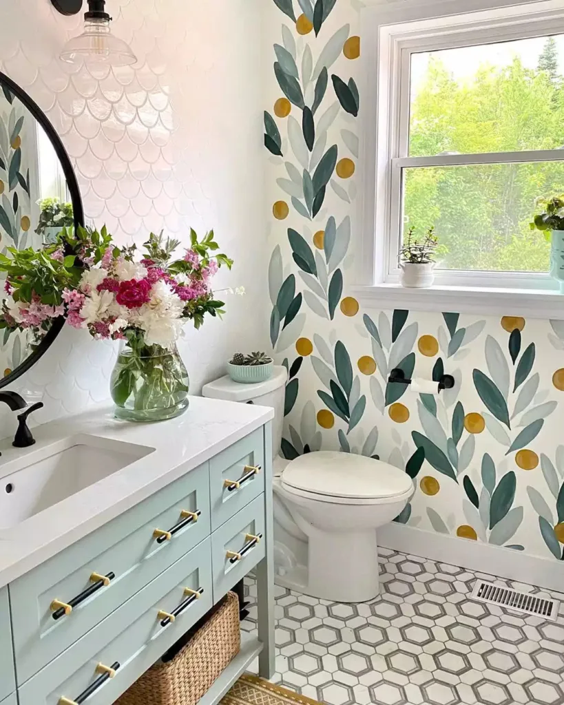 Hexagon Bathroom Floor Tiles In A Light Grey Shade Complemented By A Vibrant Floral Wallpaper On The Walls. White Subway Tiles Are Used For The Shower Area And Sink Backsplash, While The Cupboards Are Painted In A Cheerful Sky Blue Hue. A Small Flower Pot Sits On The Countertop, Adding A Touch Of Natural Beauty To The Space.