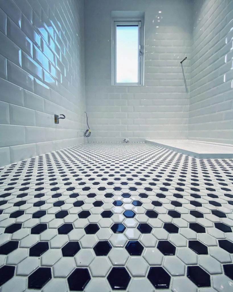 A Stylish Black And White Bathroom With Hexagonal Floor Tiles In A Classic Pattern. The Walls Are Covered In White Tiles With A Glossy Finish, Creating A Bright And Airy Atmosphere. 