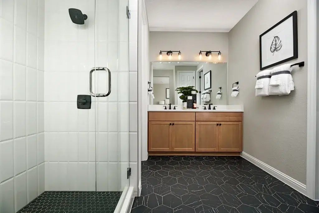 38 Bathrooms With Hexagon Tile Floors 13 A Chic Bathroom With White Walls And A Striking Black Hexagonal Tile Pattern On The Floor, Creating A Bold And Stylish Contrast. Wooden Cupboards Provide Storage And A Natural Touch, While A Painting Of Leaves On The Wall Adds A Pop Of Color And A Touch Of Artistry To The Room. The Bathing Area Is Enclosed With Glass, Providing A Sleek And Modern Touch. The Hexagonal Tiles Have A Matte Finish, Adding A Subtle Texture To The Space.
