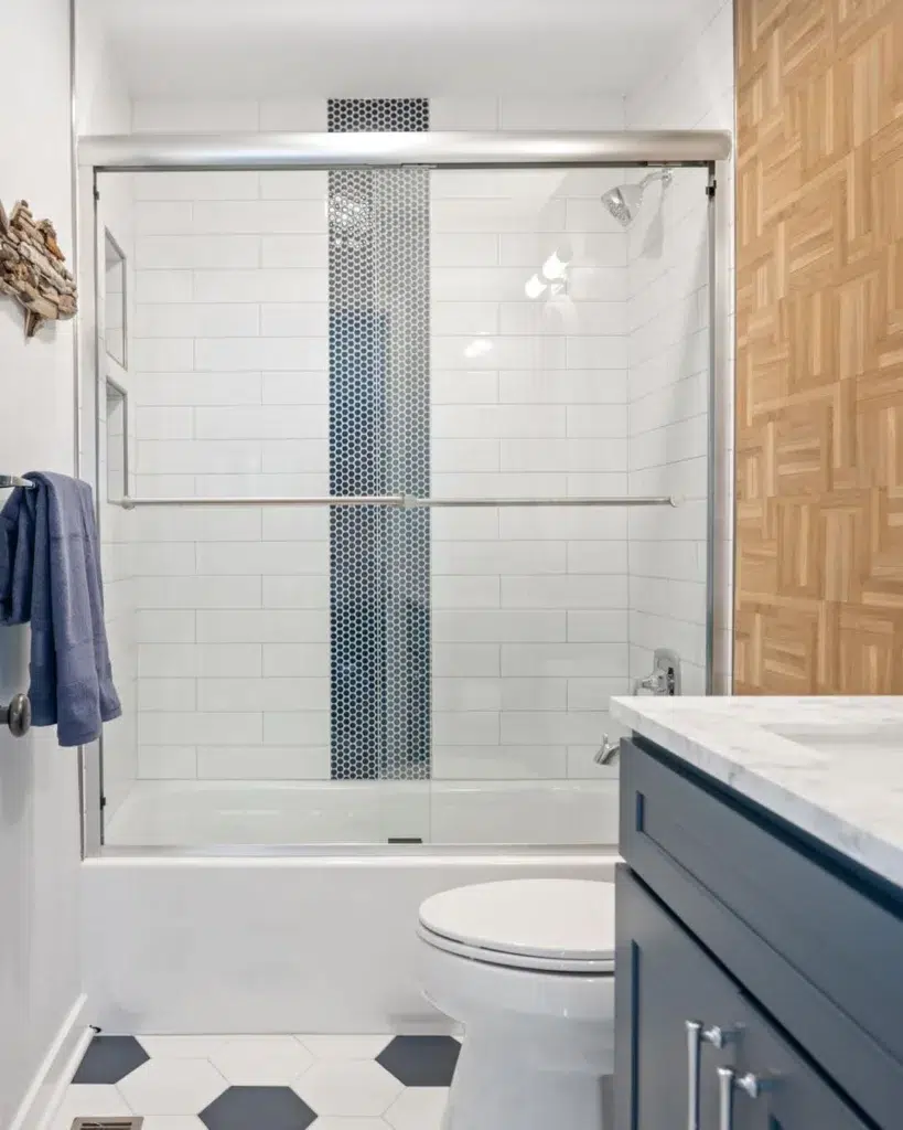 A Serene And Refreshing Bathroom With White Tiles Covering The Walls And A White Hexagon Floor. The Blue Curtains And Cupboards Add A Pop Of Color To The Space, Creating A Soothing And Calming Atmosphere. The White Tub And Toilet Seat Add A Clean And Fresh Feel To The Design, While Also Complementing The Blue Accents.