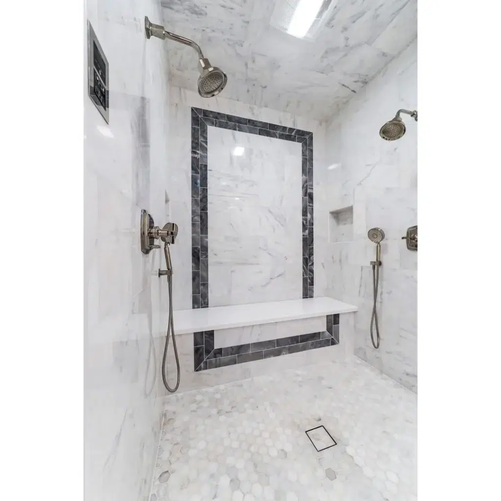 A Luxurious And Elegant Bathroom Featuring Fully White Marble Walls And White Hexagon Floors With Black Marble Outlines. The Four Hot Shower Fixtures Add A Modern Touch To The Design And Provide A Spa-Like Experience