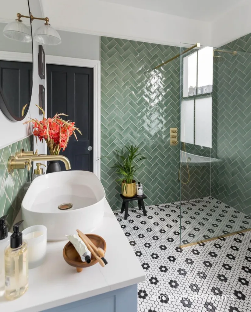 A Vibrant And Charming Bathroom With Green Tiles Covering The Walls And A Stunning Floral Hexagon Floor. The Patterned Tiles In Various Shades Of Green Add A Playful And Cheerful Element To The Space, While The White Sink And Golden Plant Vase Bring A Touch Of Elegance And Sophistication. A Black Pot With Bright Red Flowers Serves As A Striking Accent, Adding A Pop Of Color To The Design.