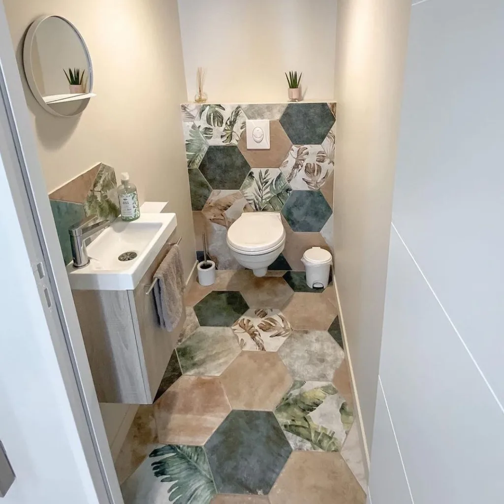 A Fun And Vibrant Bathroom Featuring A Multi-Colored Hexagonal Tile Pattern On Both The Floor And The Walls, Creating A Playful And Energetic Atmosphere. A White Toilet Seat And Sink Are Located On The Left Side Of The Space, Providing A Clean And Neutral Contrast To The Colorful Tiles. The Hexagonal Tiles Have A Glossy Finish, Adding To The Cheerful And Lively Feel Of The Room. 