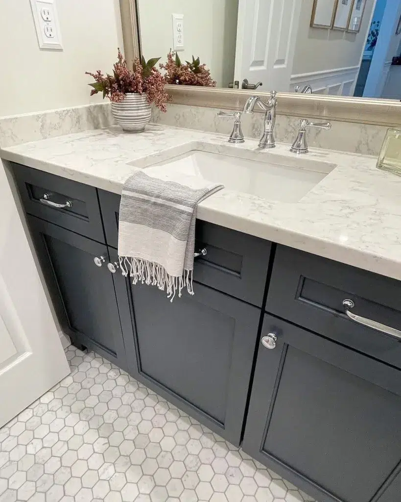 38 Bathrooms With Hexagon Tile Floors 16 A Modern Bathroom Featuring A White Hexagonal Tile Pattern On The Floor And Black Cupboards, Creating A Sleek And Stylish Contrast. The Cupboards Are Topped With A White Marble Countertop, Adding A Touch Of Luxury And Elegance To The Space. A Vase Of Flowers Adds A Pop Of Color And A Natural Touch. The Rectangular Mirror Adds A Modern And Functional Touch, Reflecting Light And Providing A Practical Space For Grooming.
