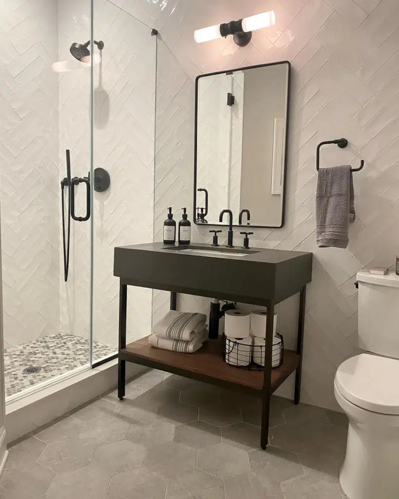 38 Bathrooms With Hexagon Tile Floors 20 A Modern And Sleek Bathroom Featuring A Grey Hexagonal Tile Pattern On The Floor And White Tiles With A Black Border, Creating A Clean And Contemporary Look. A Mirror On The Wall Is Accompanied By A Table In Front, Providing A Practical Space For Grooming. Shampoo, Conditioner, And A Black Tap Are Within Easy Reach, Adding To The Functionality Of The Space.