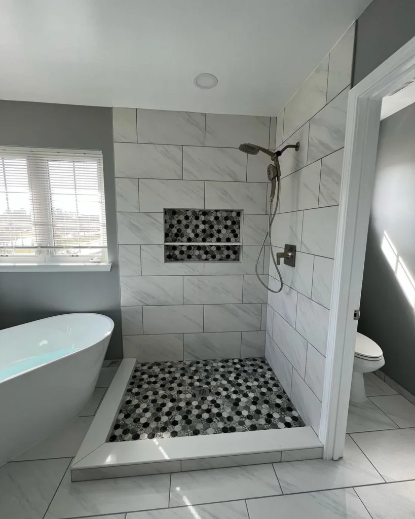 A Chic And Sophisticated Bathroom Featuring Hexagonal Tiles In A White And Light Grey Color Scheme On The Floor, Creating A Subtle Yet Stylish Pattern. A White Tub Is Situated In The Center Of The Room, Surrounded By The Hexagonal Tiles, Creating A Stunning Focal Point. A White Toilet Is Located Off To The Side, Providing Functionality And Convenience. 