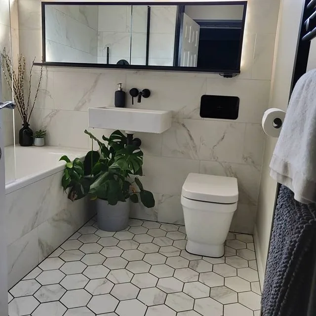 38 Bathrooms With Hexagon Tile Floors 18 A Luxurious Bathroom Featuring A White Hexagonal Tile Pattern On The Floor And White Marble Walls, Creating A Sense Of Opulence And Grandeur. Plants Add A Natural Touch And A Pop Of Greenery To The Space. The Bathtub Is A Focal Point, With A Sleek And Modern Design That Adds To The Luxurious Feel Of The Room. A Black Mirror Provides A Striking Contrast, Adding A Touch Of Drama To The Space. The Hexagonal Tiles Have A Polished Finish, Reflecting Light And Adding To The High-End Feel Of The Room.