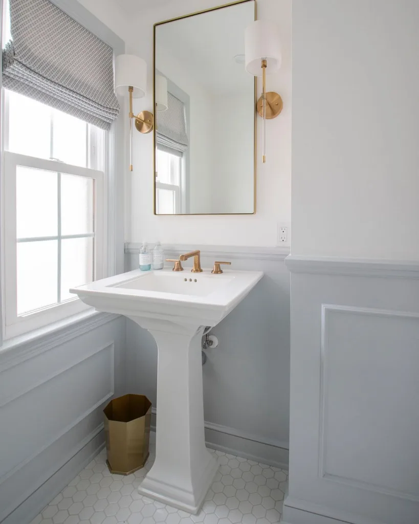 38 Bathrooms With Hexagon Tile Floors 26 A Bright And Airy All-White Bathroom Featuring White Tiles On The Walls And A White Sink, Creating A Clean And Refreshing Look. The Hexagonal Tile Pattern On The Floor Is Also White, Adding To The Sense Of Spaciousness And Lightness In The Room. A Bathroom Mirror With A Border Of Golden Trim Is Located Above The Sink, Adding A Touch Of Elegance And Refinement To The Space.
