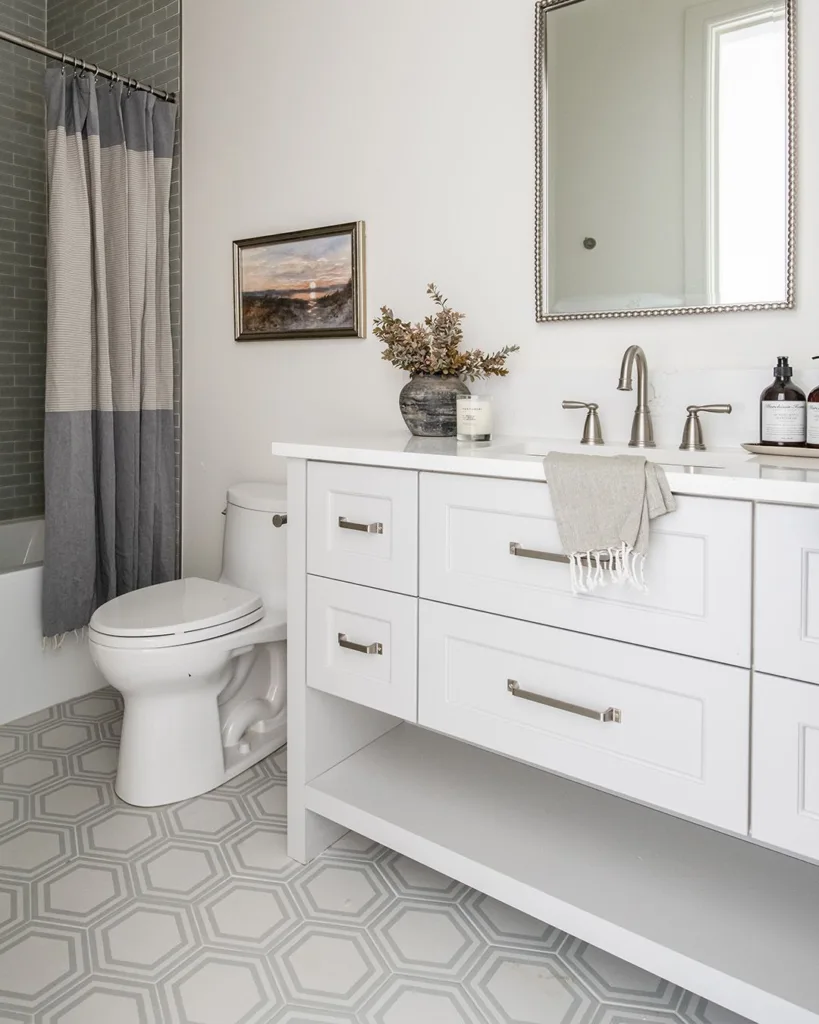 A Bathroom With Cream-Colored Hexagonal Tiles Covering The Floor, Creating A Warm And Inviting Atmosphere. The Bathing Area Features A Glass Enclosure, Providing A Clear Separation Between The Shower And The Rest Of The Bathroom. The Door Is White, Providing A Clean And Modern Touch.