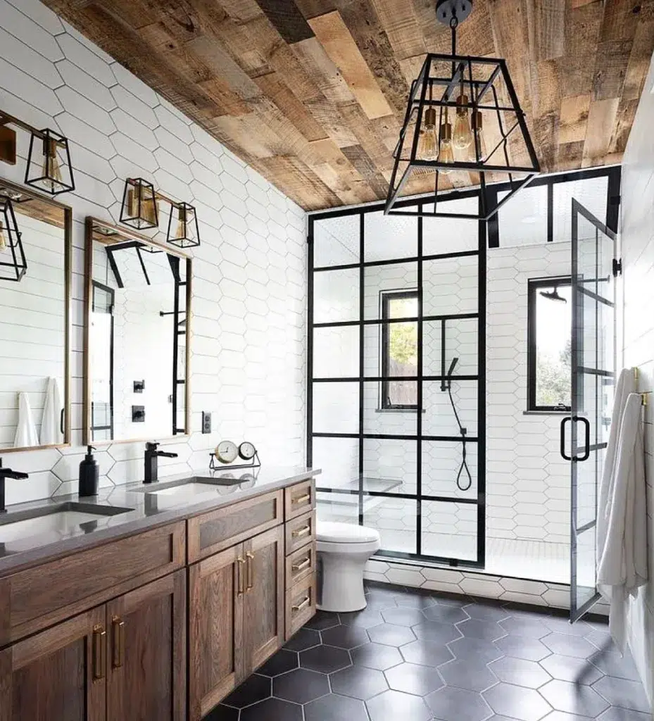 A Stylish Bathroom With A White Hexagonal Tile Pattern On The Floor, Creating A Classic And Timeless Look. Black Railings Surround The Bathing Area, Providing A Sleek And Modern Touch. The Glass Door Adds To The Minimalist And Elegant Feel Of The Space. The Ceiling Is Covered In Wooden Planks, Creating A Warm And Inviting Atmosphere. The Hexagonal Tiles Have A Glossy Finish, Adding A Subtle Sheen To The Room.